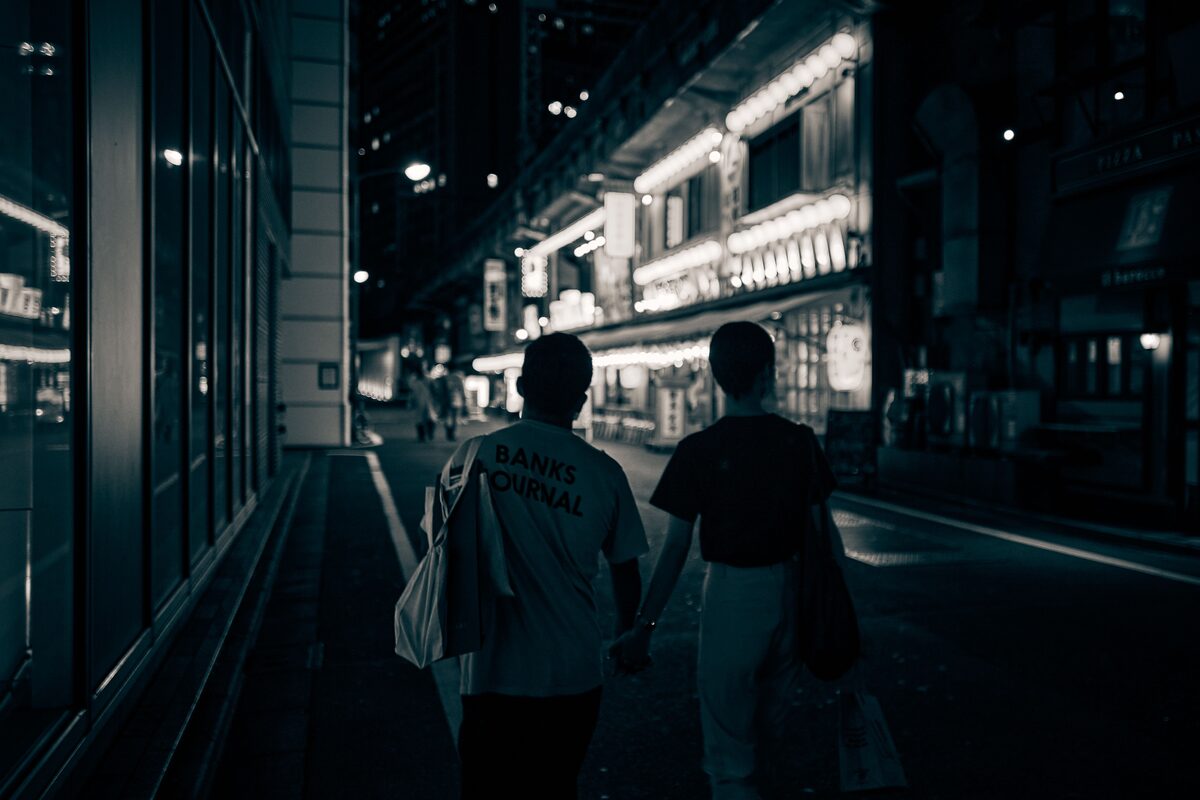 A couple walking along a bright, neon-lit street at night, holding hands and enjoying the city ambiance.