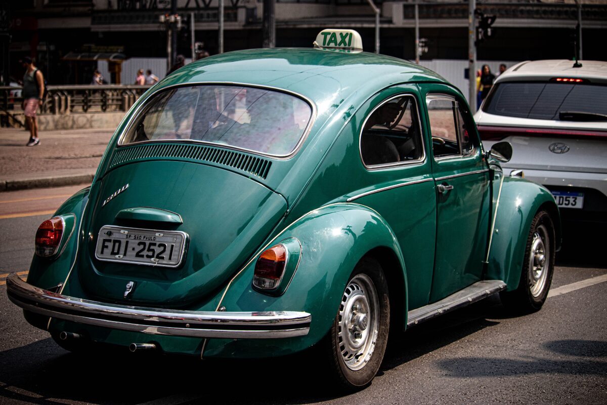 Classic green Volkswagen Beetle taxi on a busy street in São Paulo, Brazil.