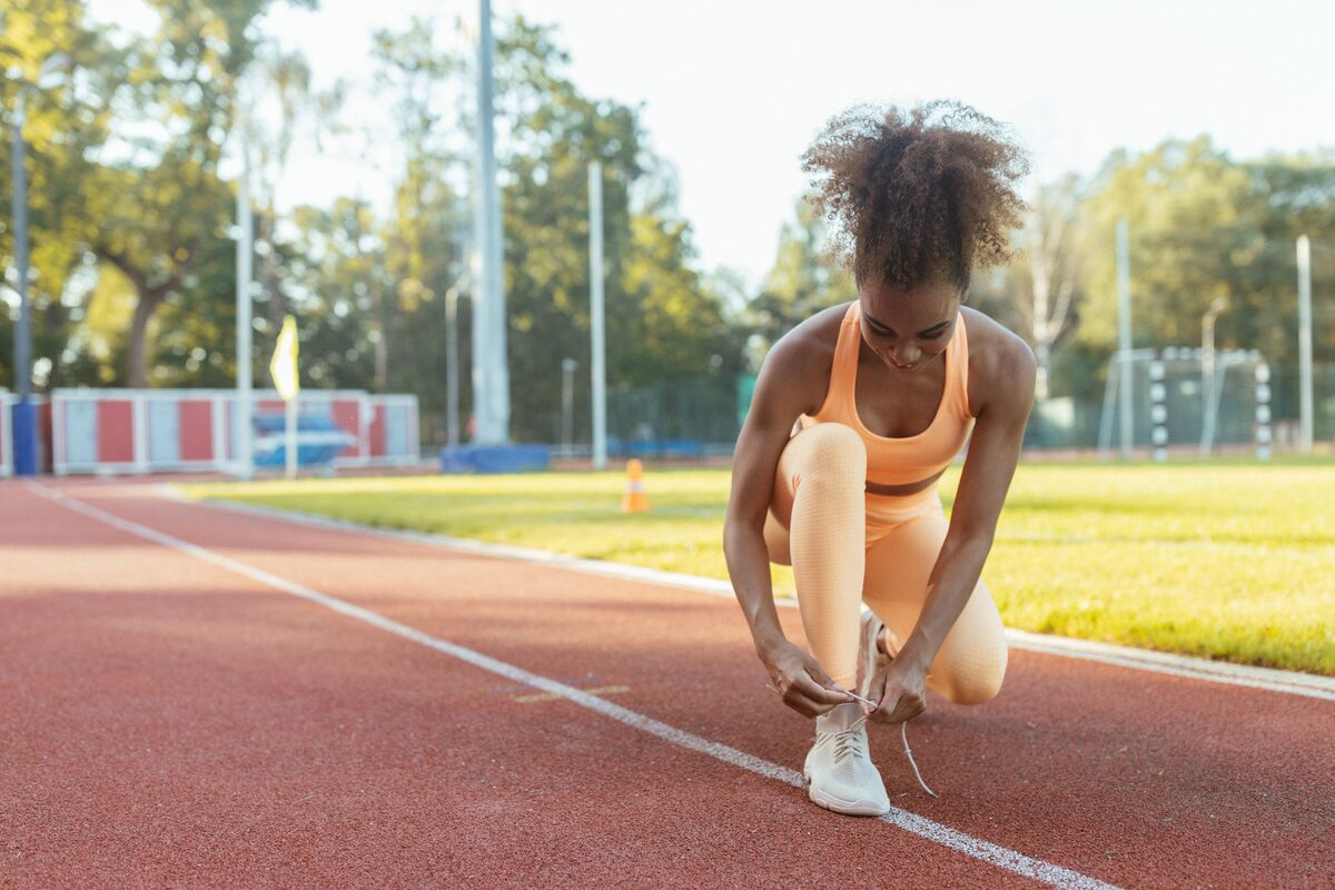 A fit young woman ties her shoes on an outdoor running track, ready for exercise.