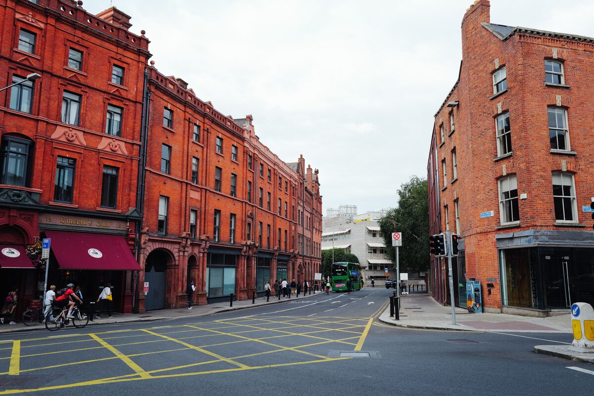A bustling urban street with red brick buildings and a green bus passing by.