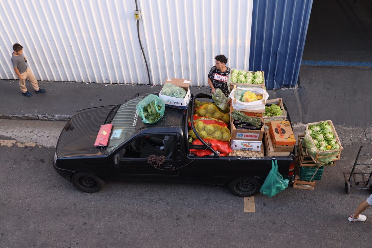 Black truck filled with various fresh vegetables parked on city street, viewed from above.