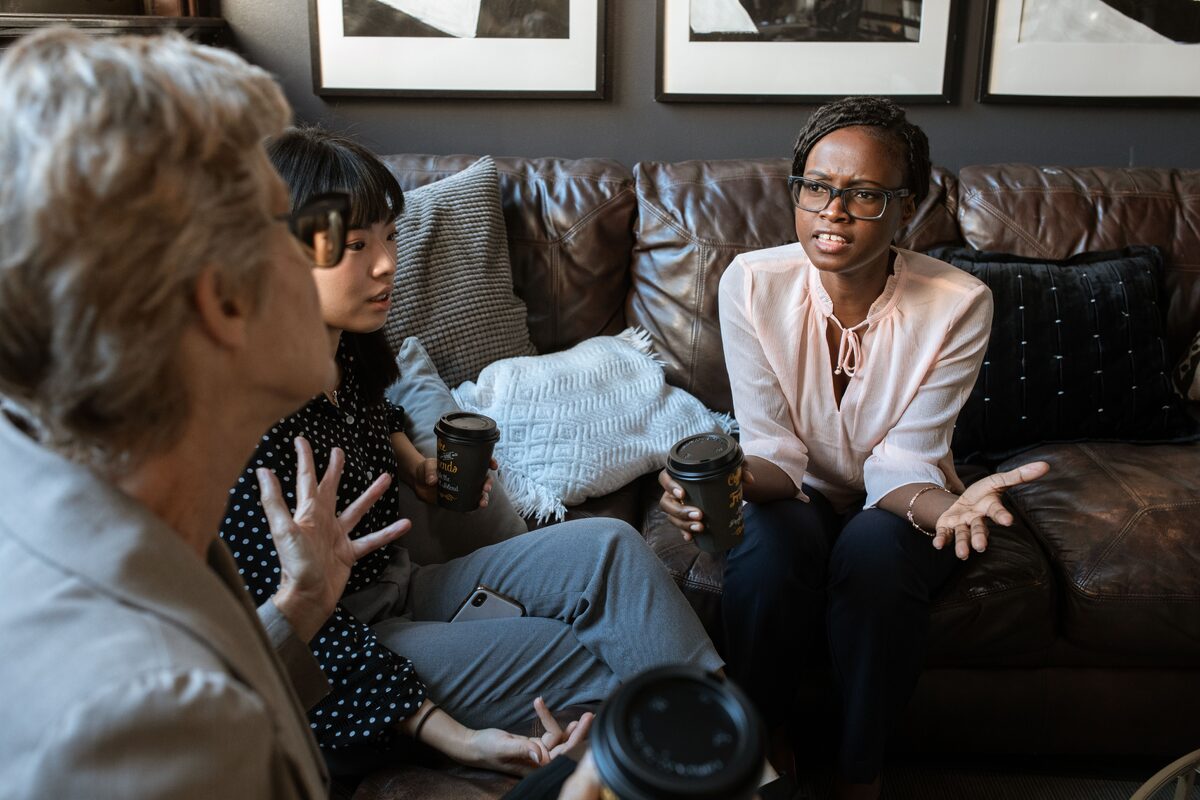 Three diverse entrepreneurs discussing ideas over coffee in a modern workspace.