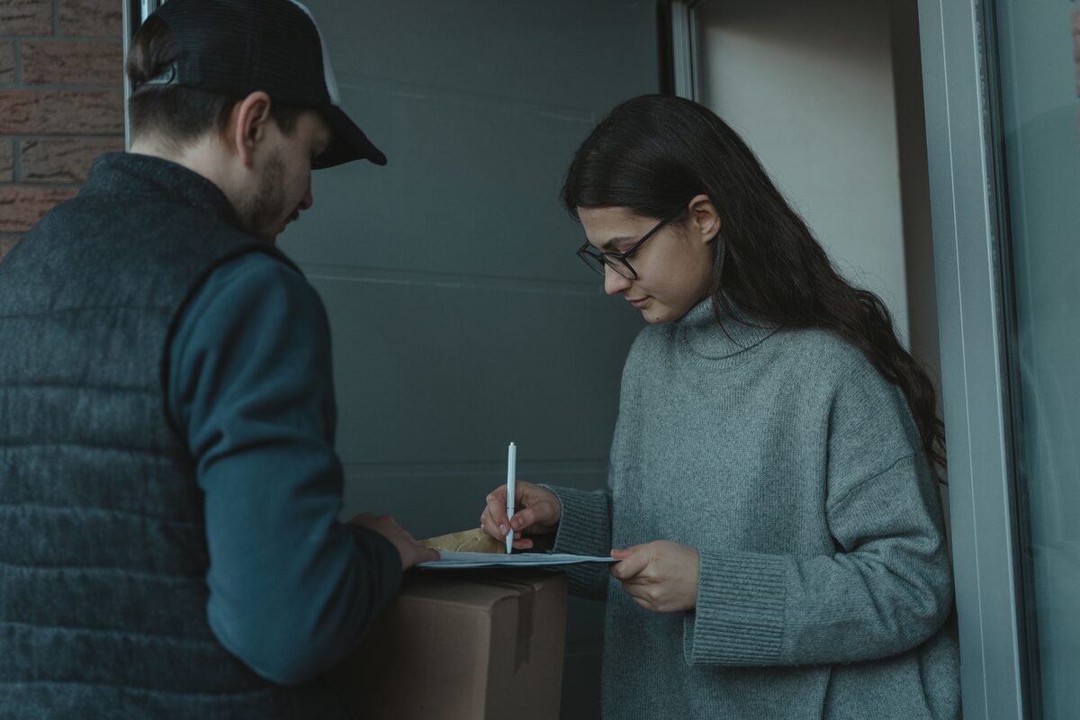 A woman signs for a package delivered by a courier at her doorstep, showcasing home delivery service.