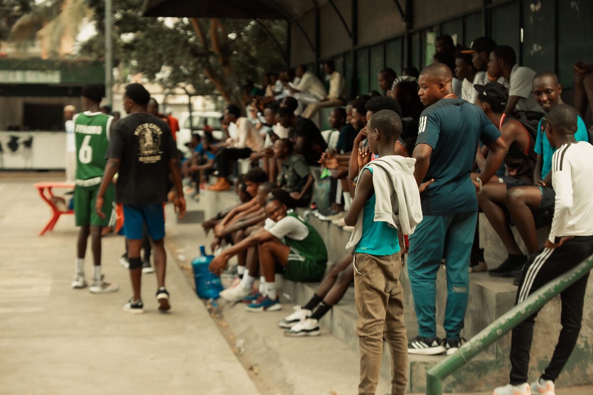 Crowd gathered at an outdoor basketball game, observing players on the court.