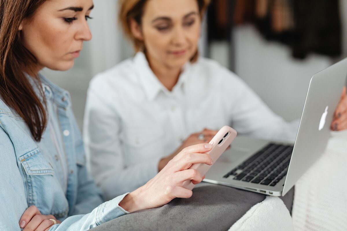 Two women working together using a laptop and smartphone in a casual setting.