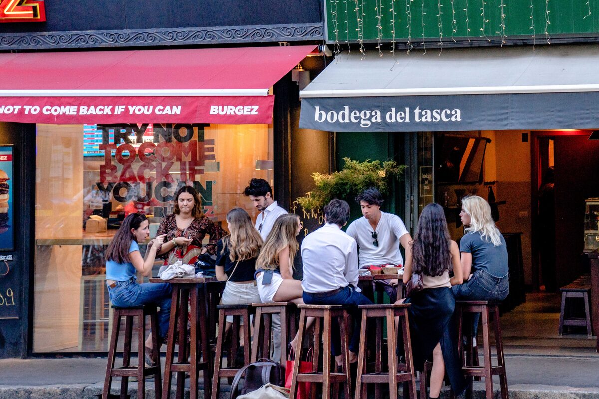 Friends enjoying a meal outside Bodega del Tasca in Milan's vibrant street setting.