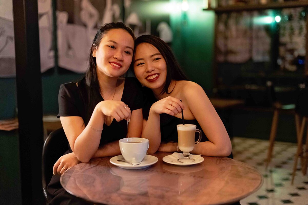 Two smiling Asian women enjoying coffee at a cozy café, showcasing friendship.