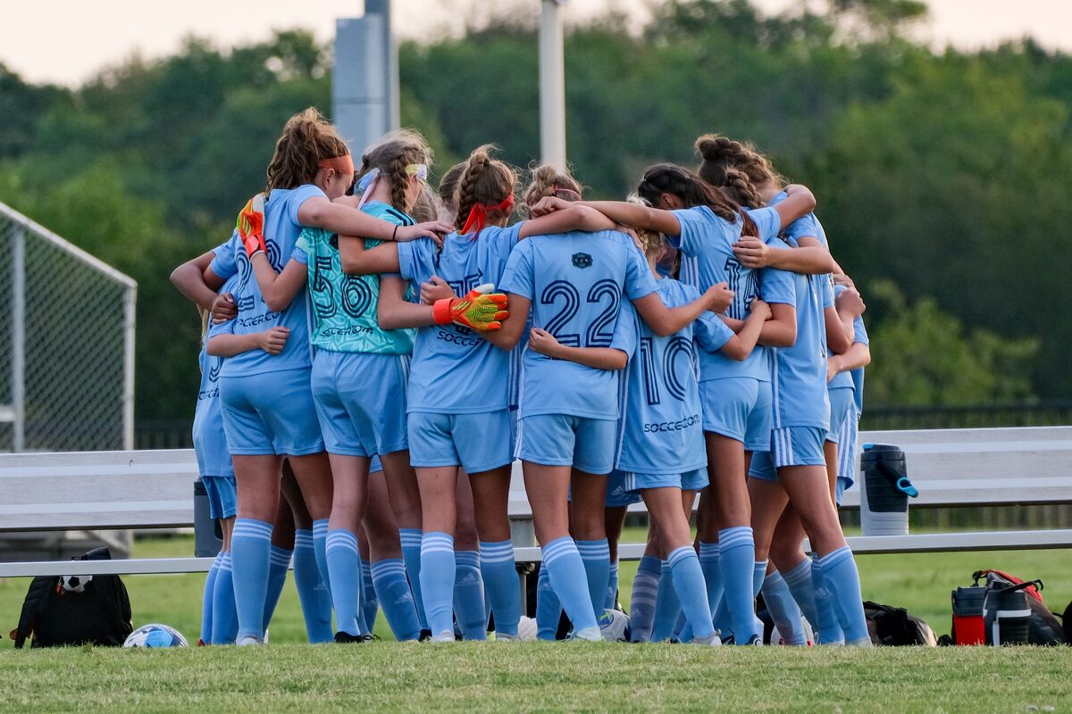 A girls' soccer team huddles together in a circle before a match, promoting teamwork and unity.