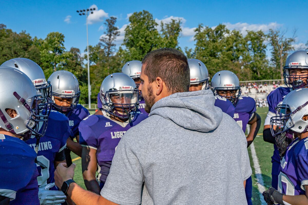 A coach leads a football team huddle during a game outdoors in Columbia.