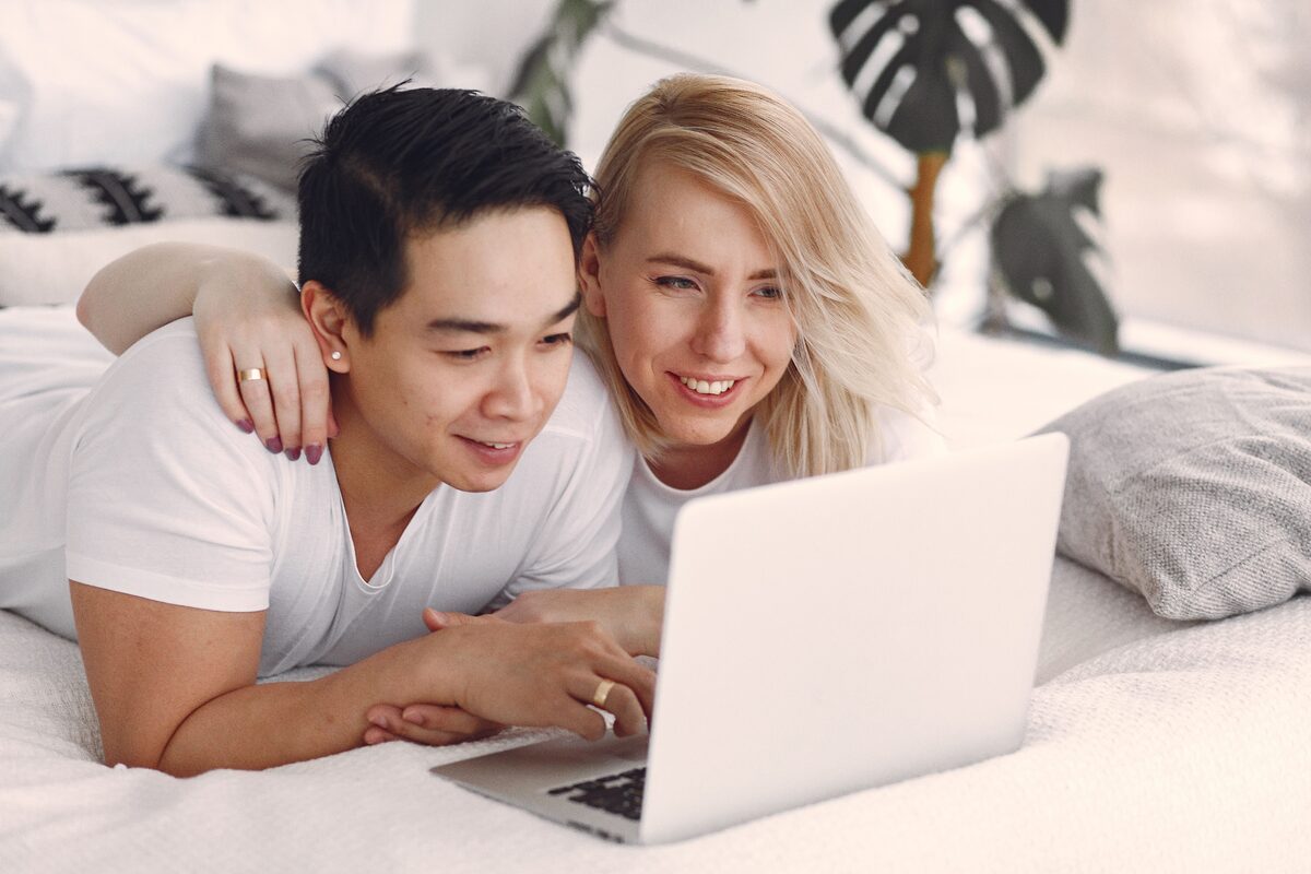 Happy couple streaming video together on a laptop indoors, enjoying relaxed leisure time.
