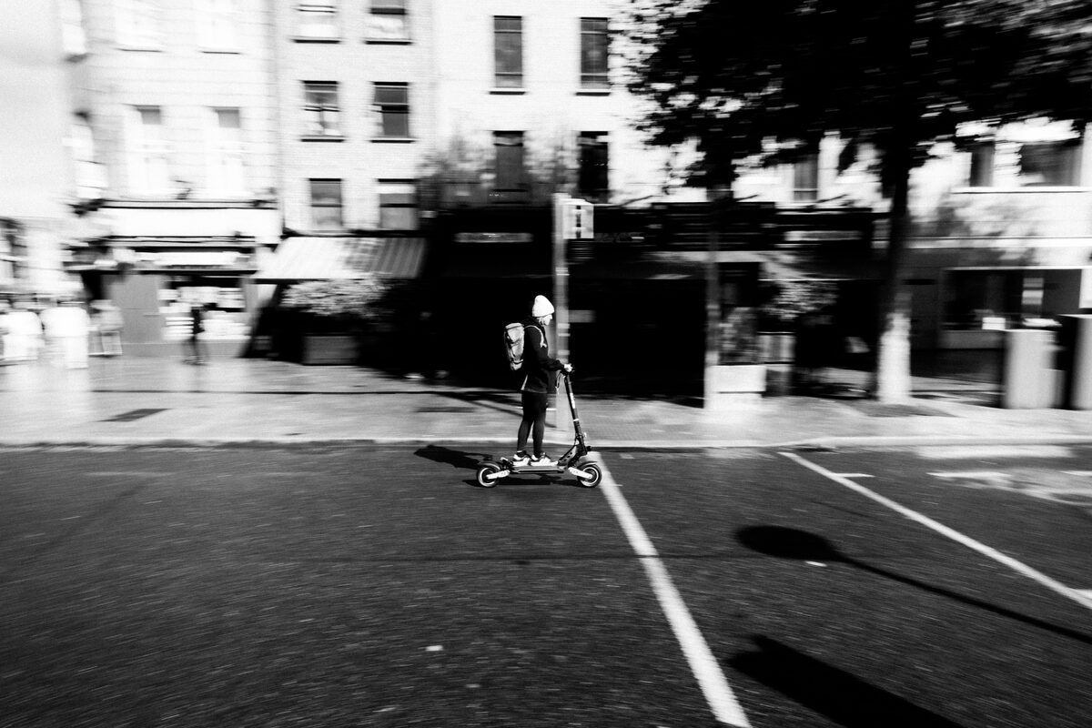 Black and white image of a person riding an e-scooter on a city street in Dublin, Ireland.