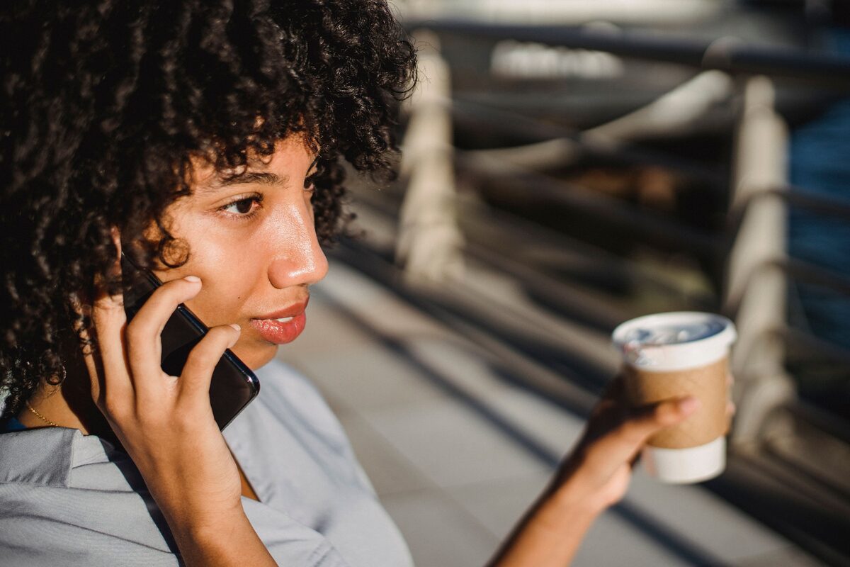 African American woman with curly hair having a phone conversation while holding a coffee cup.