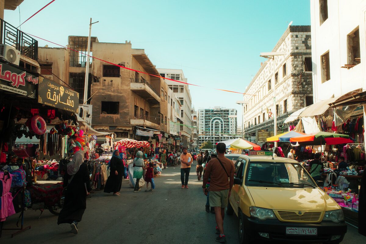 Vibrant street market scene in Homs, Syria with people shopping amidst colorful stalls.