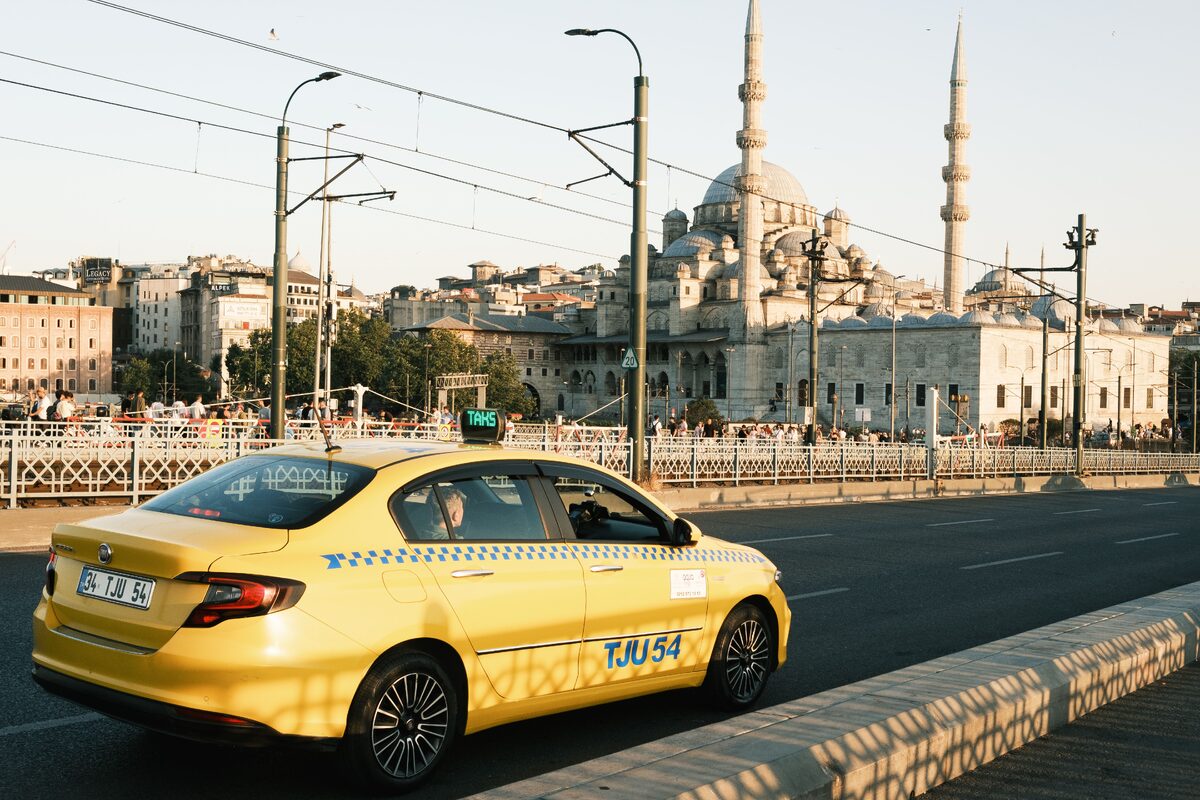 Yellow taxi driving across a bridge in Istanbul with a view of the iconic Yeni Mosque in the background.