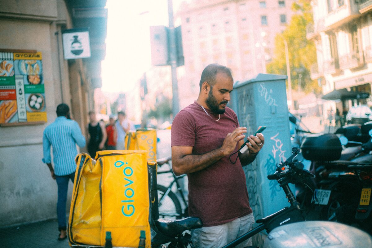 Delivery courier using his phone next to bicycle in a sunny urban street.