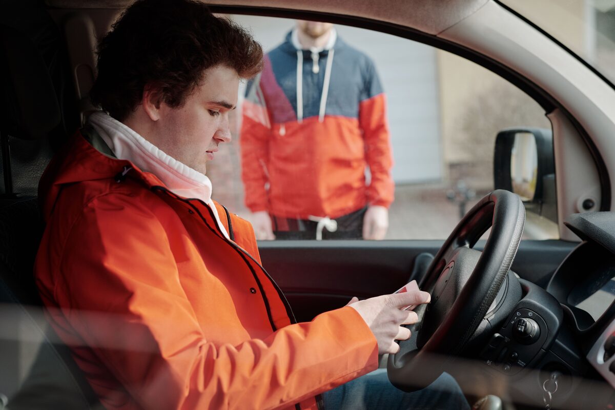 Young man in orange jacket using smartphone inside a car, highlighting modern lifestyle and technology.