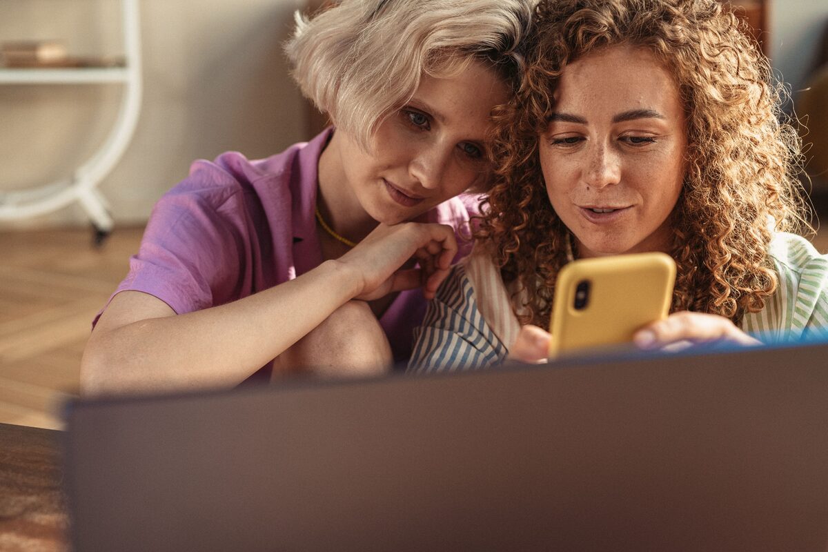 Two friends enjoying a moment indoors, interacting with a smartphone in a cozy setting.
