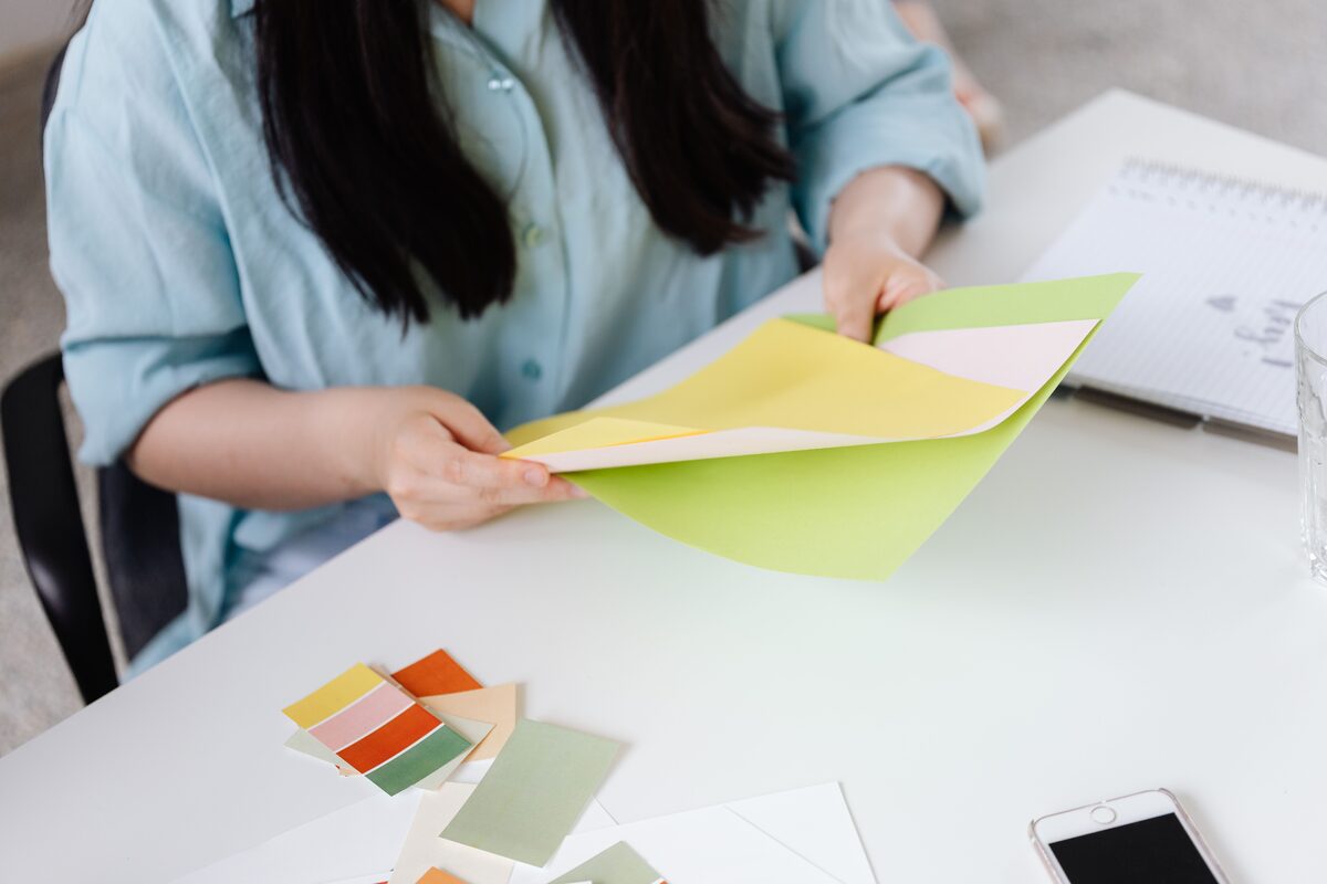 Designer examining color paper samples on a white desk with creative materials.