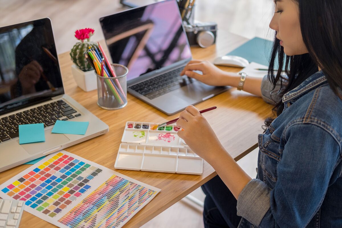 A woman using a laptop and painting with watercolors in a modern office environment.