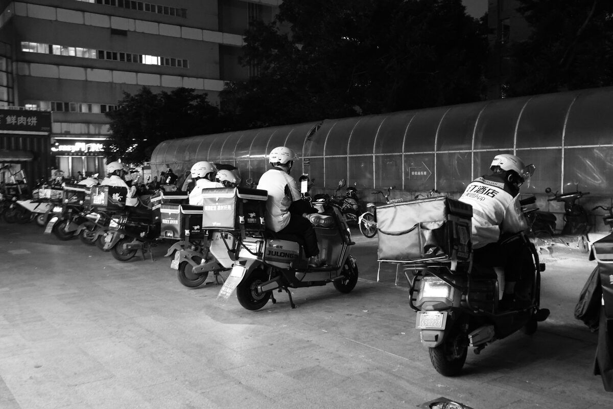 Food delivery drivers on scooters gather at night for dispatch in an urban setting.