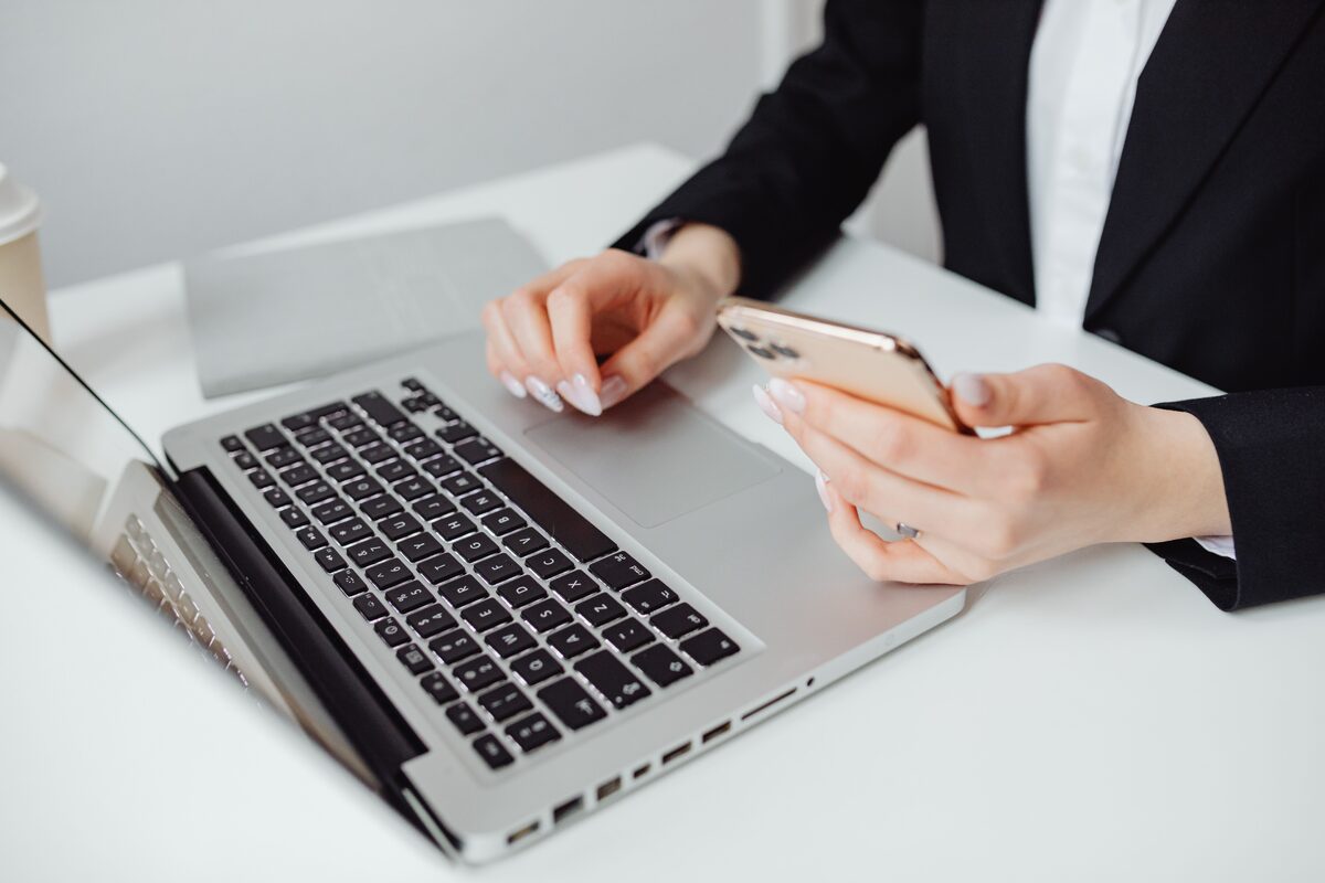 Professional woman in business attire using a laptop and smartphone at a desk.