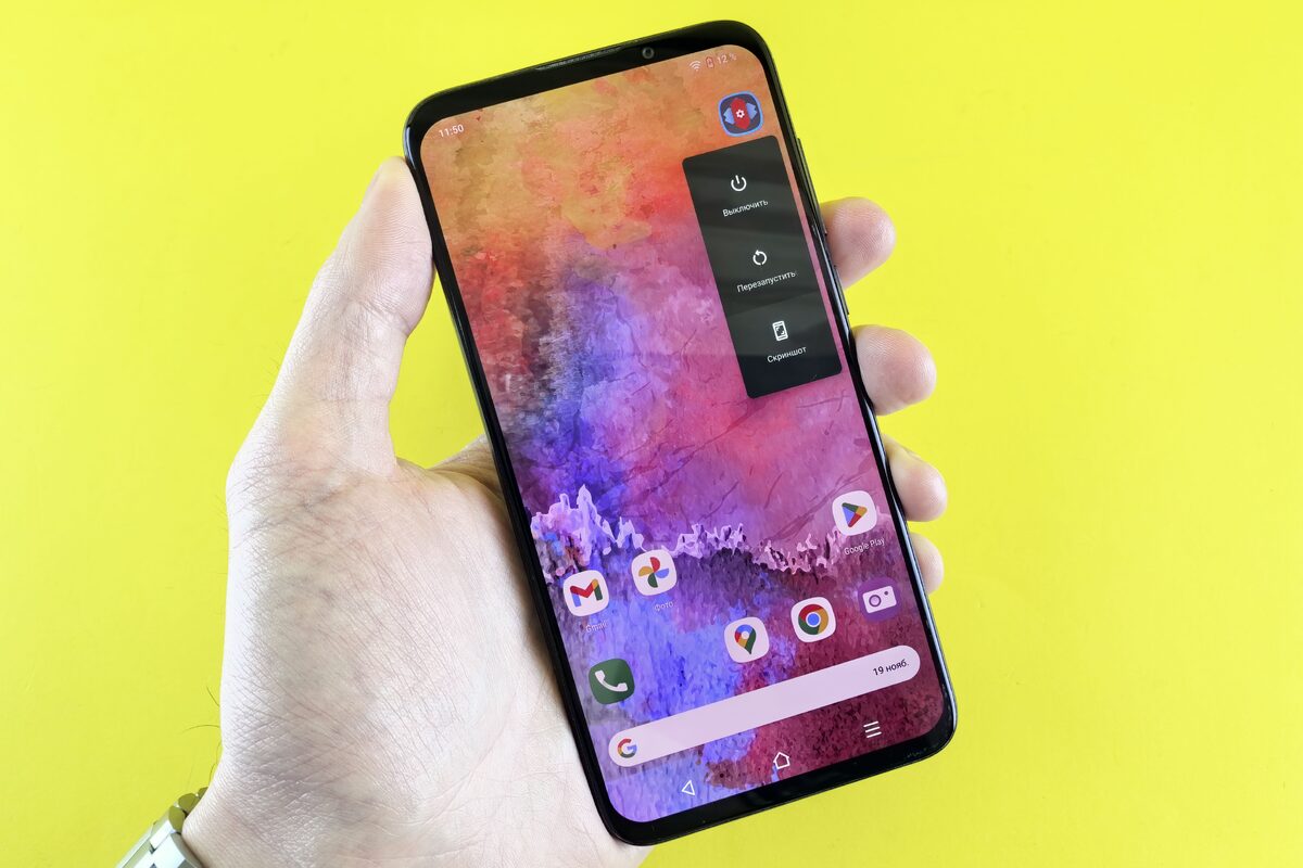 A close-up of a hand holding a smartphone with a colorful abstract wallpaper against a yellow background.