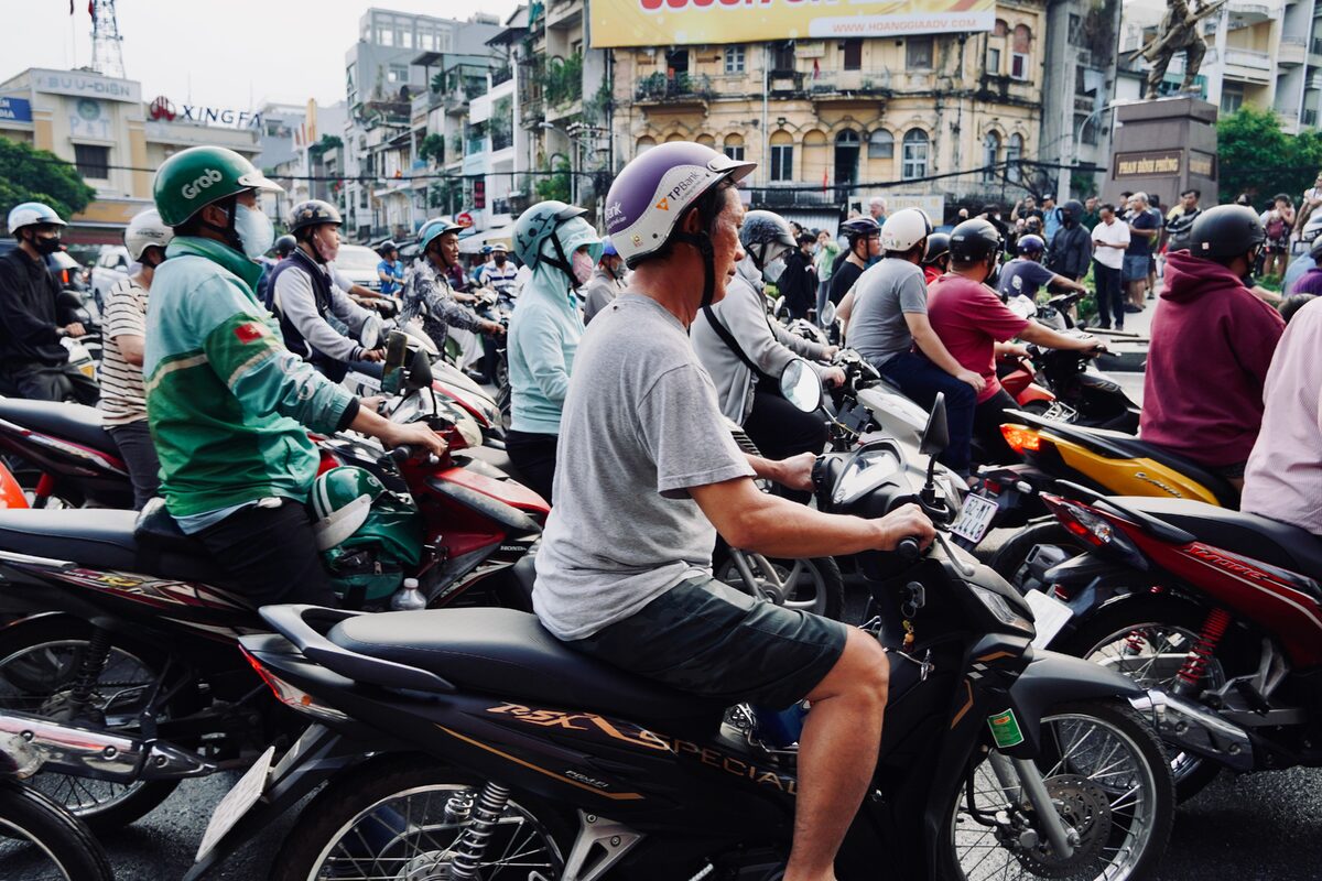 A busy urban street scene with numerous motorcyclists waiting at a traffic light.