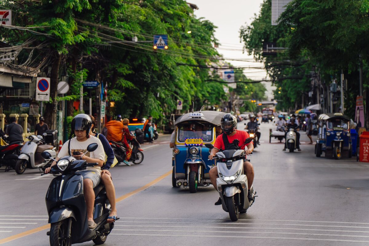 A vibrant Bangkok street scene with motorbikes and tuk tuks in motion during the day.