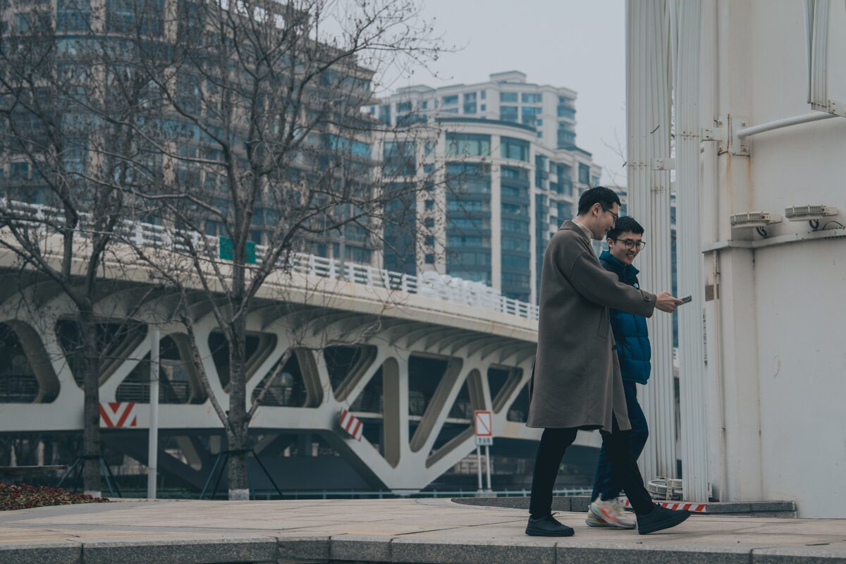 Two men walking near a modern bridge in a cityscape, enjoying a leisurely day outdoors.