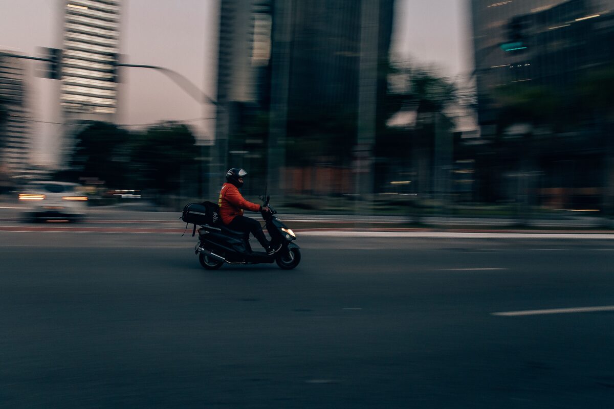 Blurred motion of a delivery scooter on São Paulo street at dusk, capturing urban hustle.
