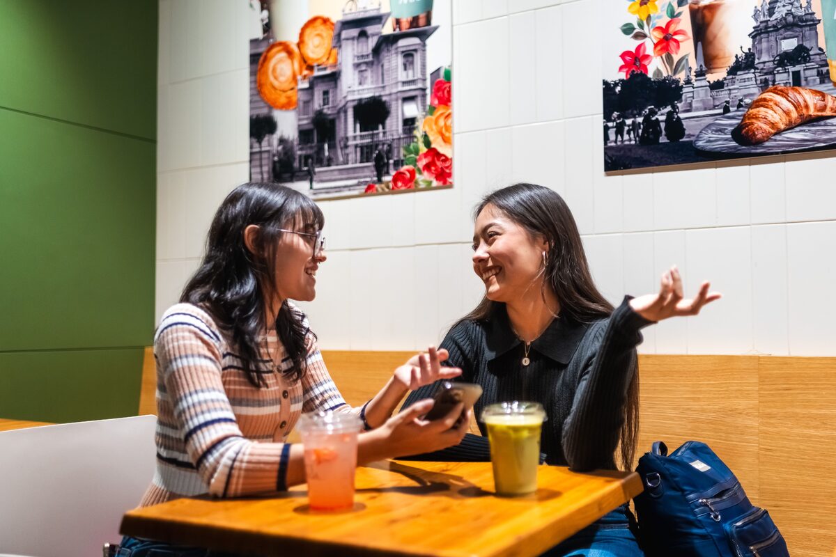 Two women enjoying a conversation over drinks in a cozy café, surrounded by vibrant wall art.