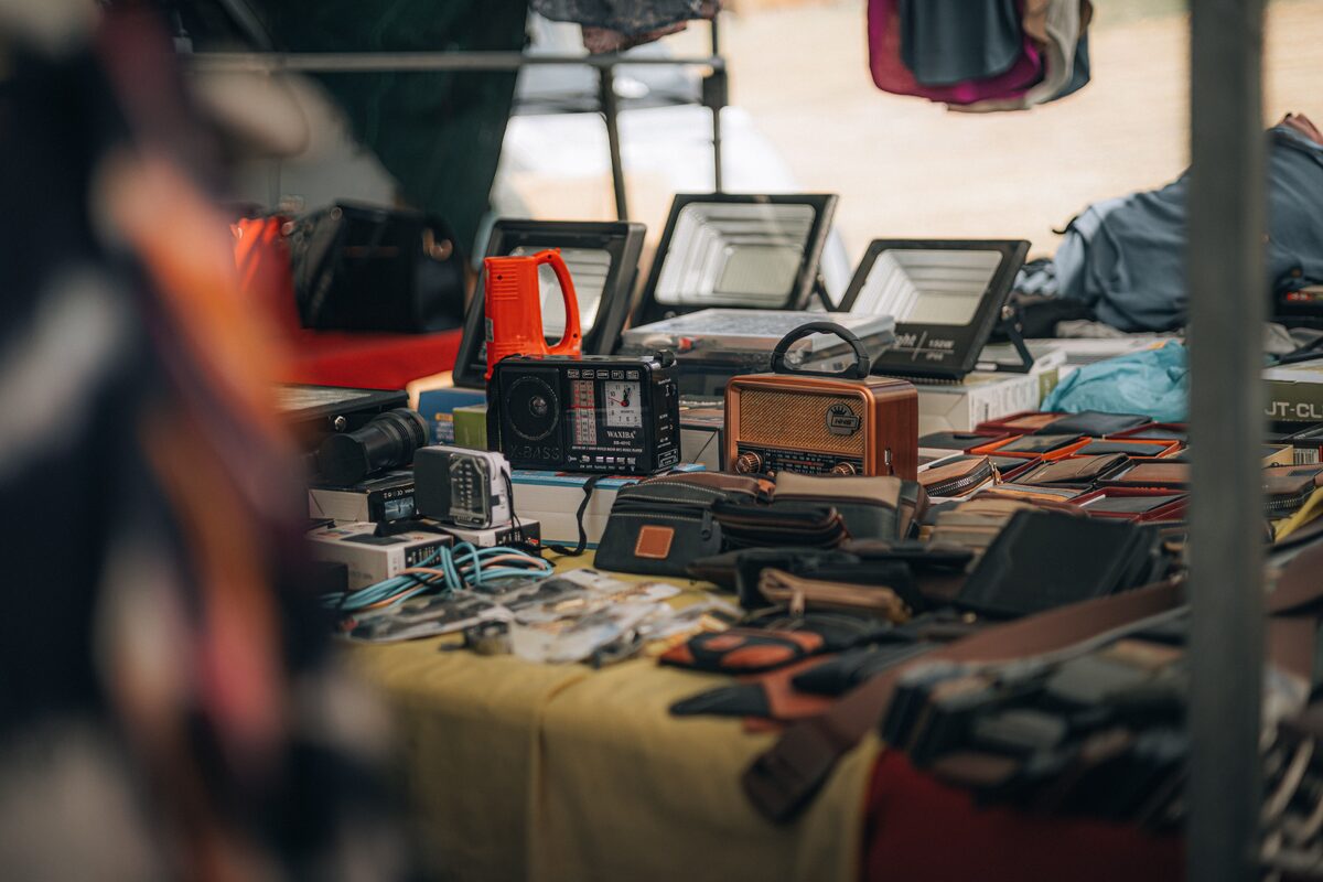 A tabletop display of vintage radios, gadgets, and leather goods at an outdoor flea market.