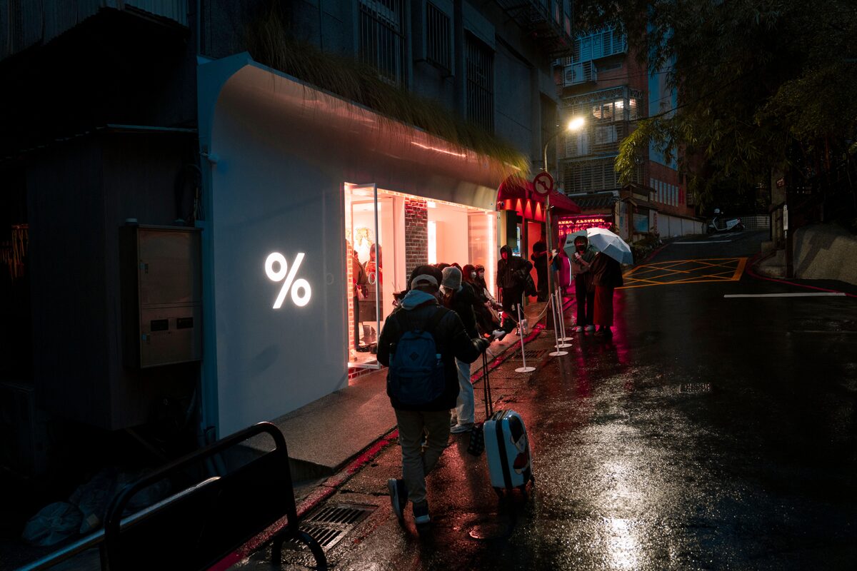 People waiting outside an illuminated store on a rainy evening in the city.