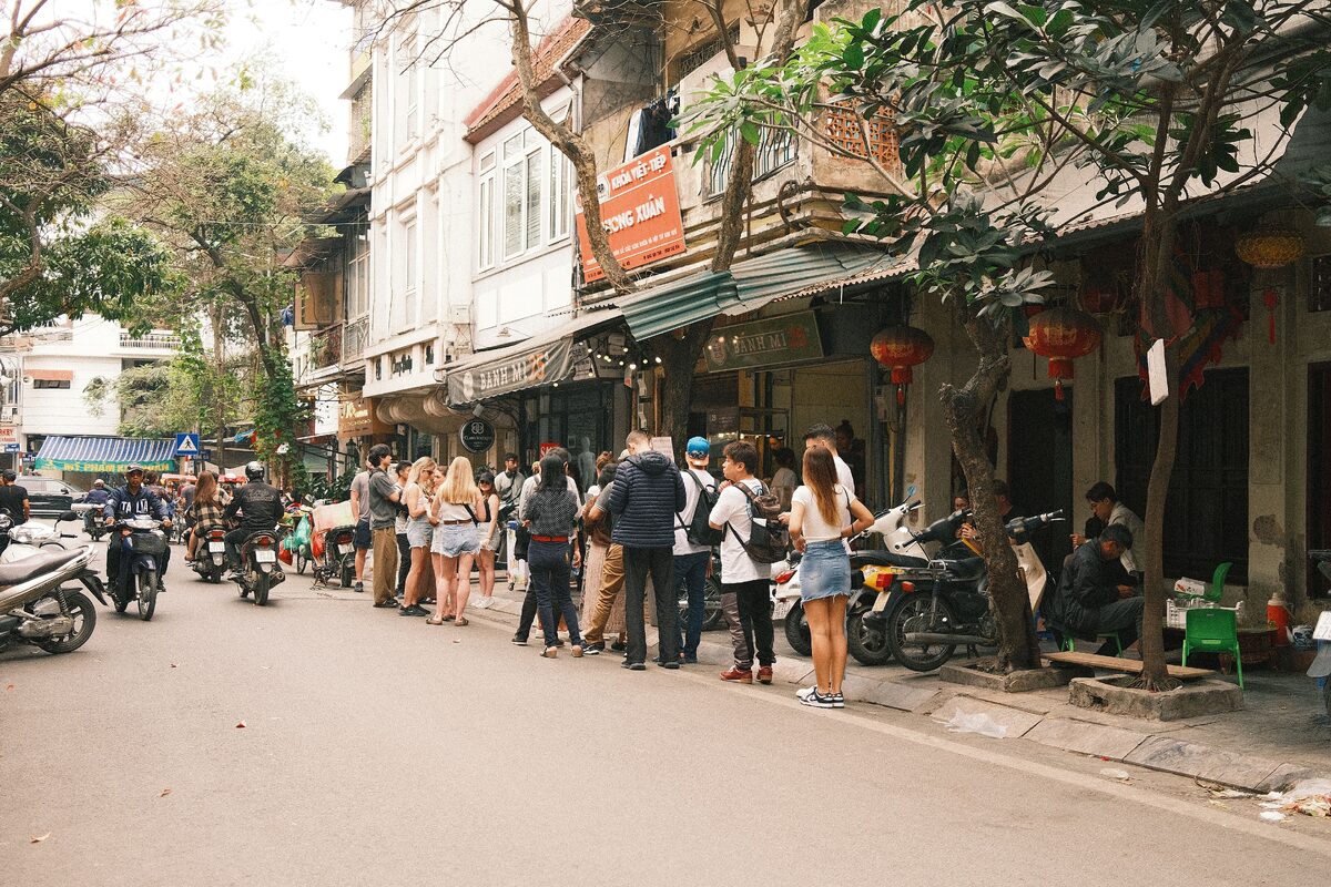 Bustling street scene in Hanoi featuring people lined up outside a shop, capturing the lively atmosphere.