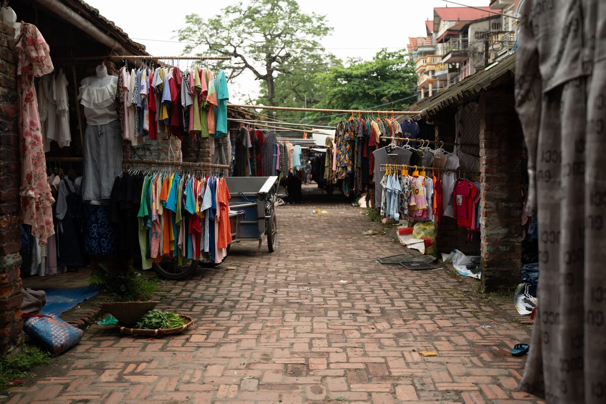 Outdoor market street showcasing vibrant clothing displays hanging in rows, ideal for commerce and tourism.