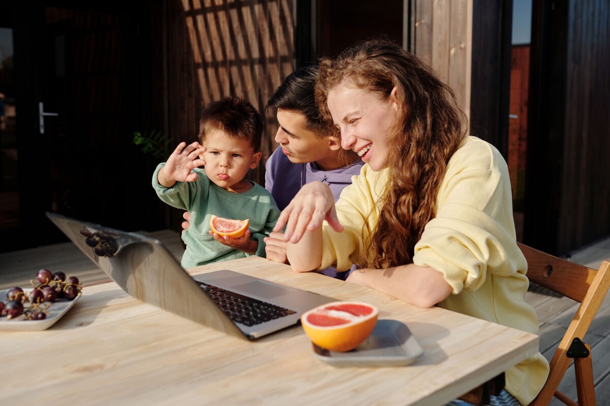 A family sitting outside enjoying a video call on a laptop, sharing smiles and fresh fruit.