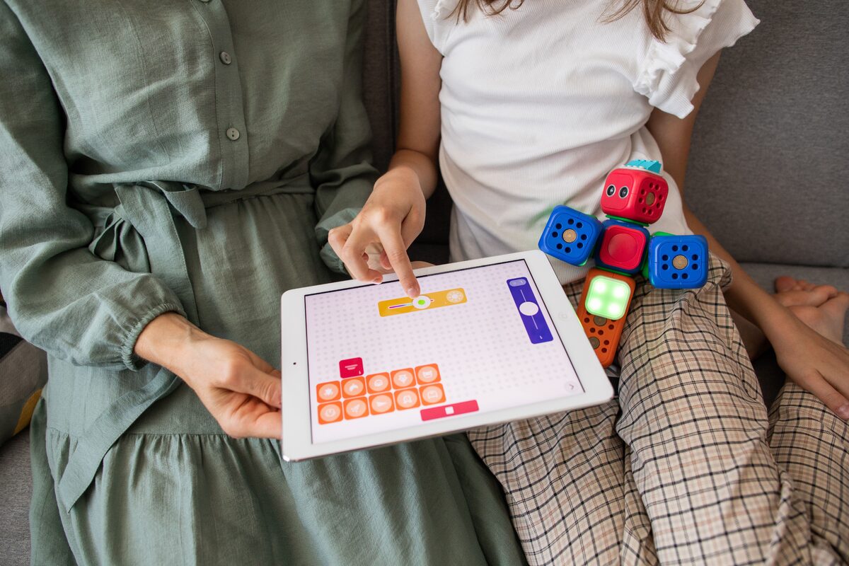 A child and parent using a tablet together at home, learning and playing with a colorful robot toy.