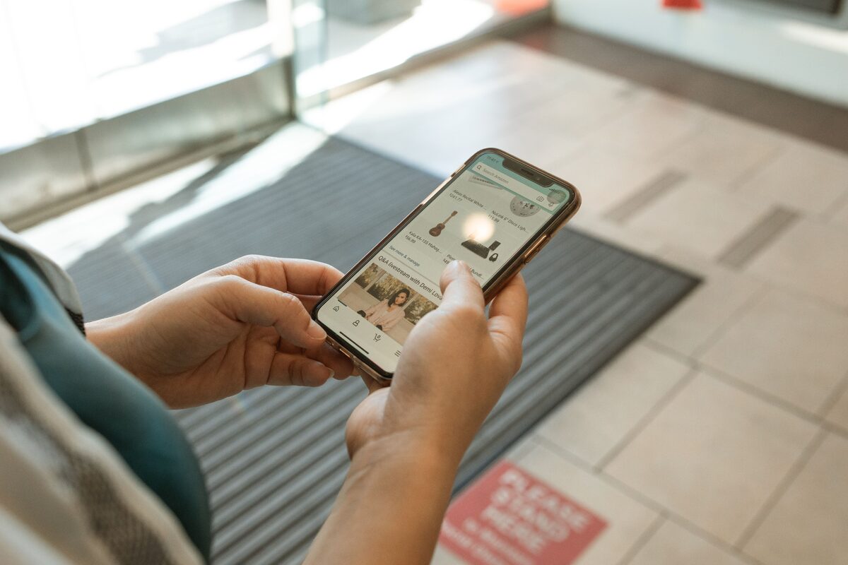 Close-up of hands holding a smartphone displaying an online shopping app in an indoor setting.