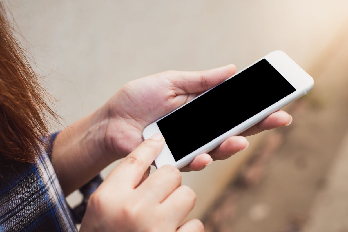 A hand holding a phone with a blank screen, seen over a desk