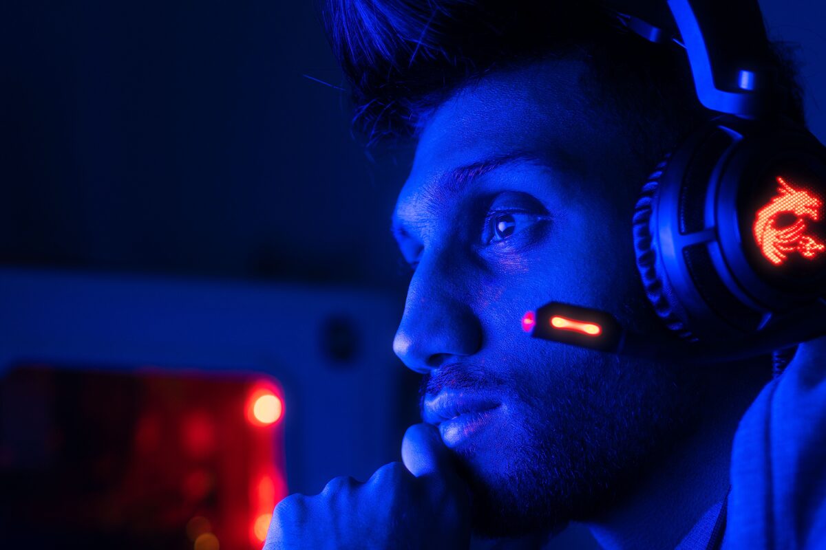 Close-up of a focused gamer with headset in blue lighting, embodying intense concentration.