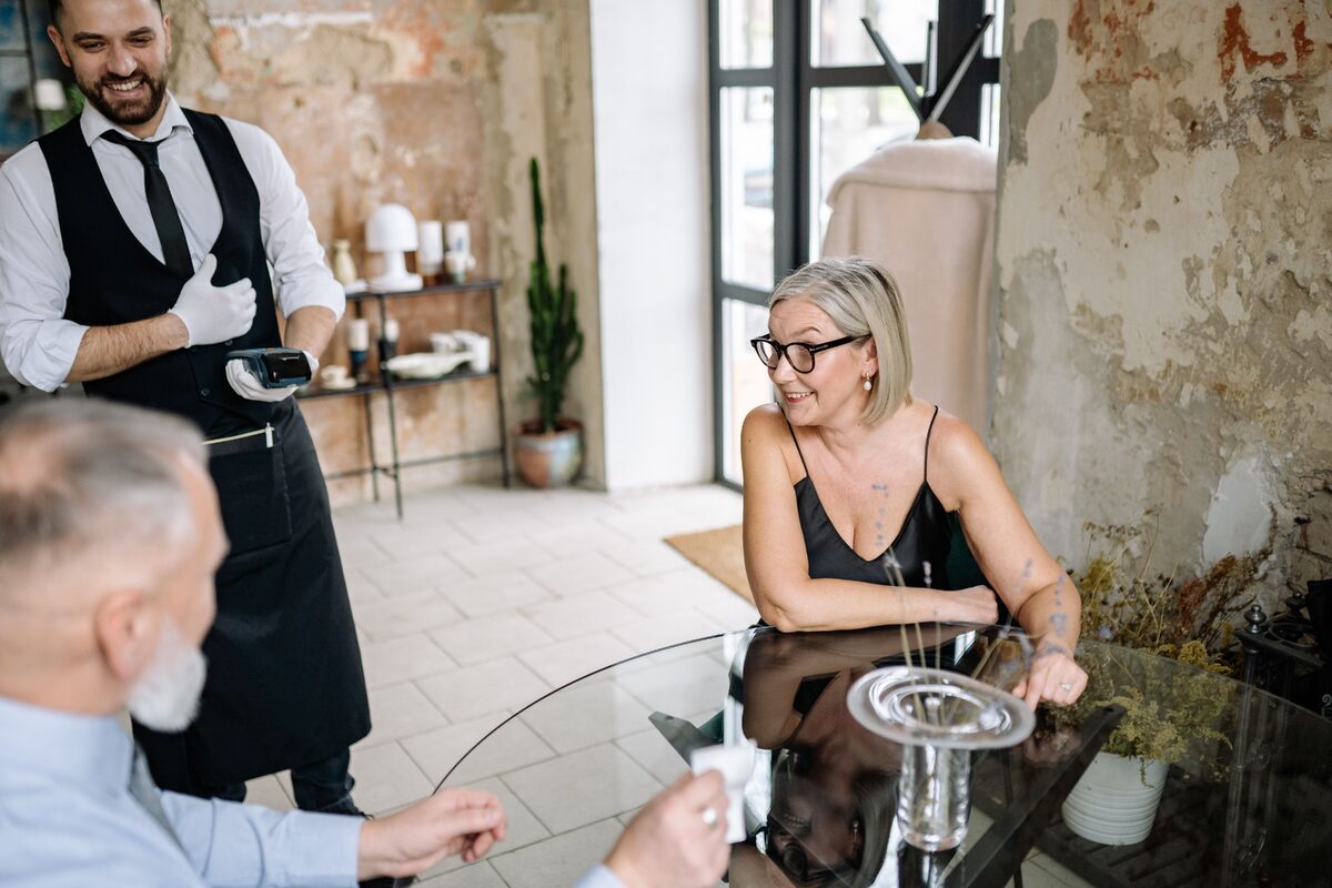 A waiter serves a senior couple in a rustic café, highlighting elegance and enjoyment.