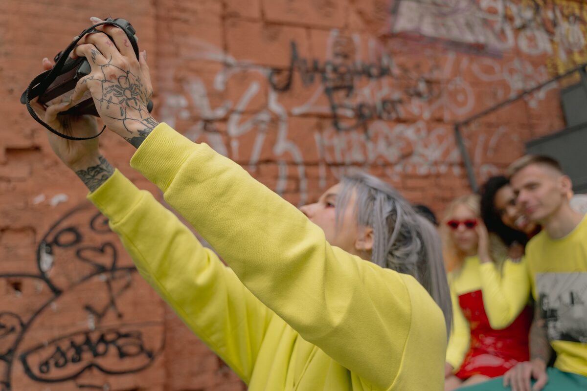 A group of stylish friends taking selfies against a graffiti-covered wall, showcasing urban street fashion.