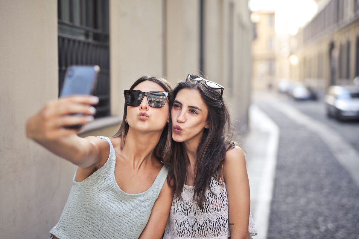 Two young women enjoying a moment together, taking a selfie in a sunny urban alley.