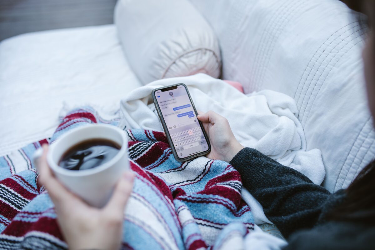 A person sitting with a coffee, reading messages on a phone