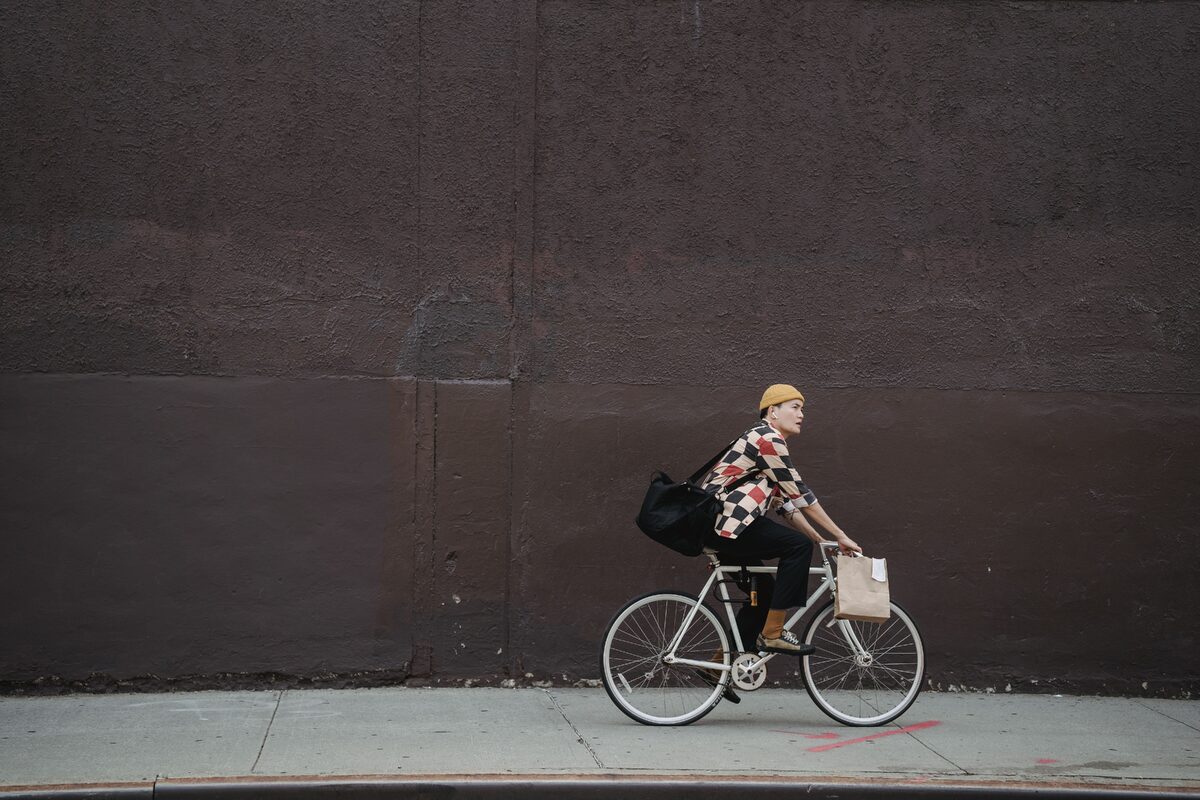 A courier riding a bicycle with bags along a city street against a concrete wall.