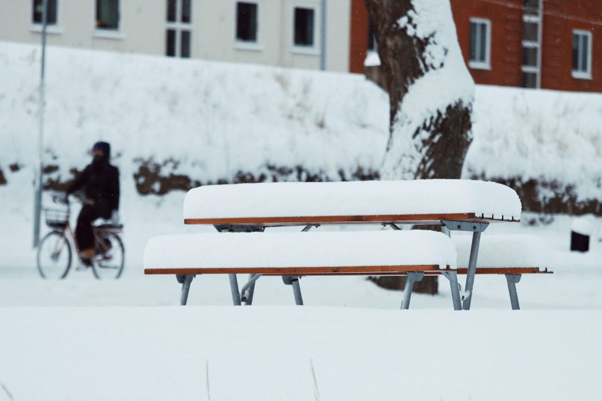A snow-covered bench in Jönköping, Sweden with a cyclist passing by in winter.