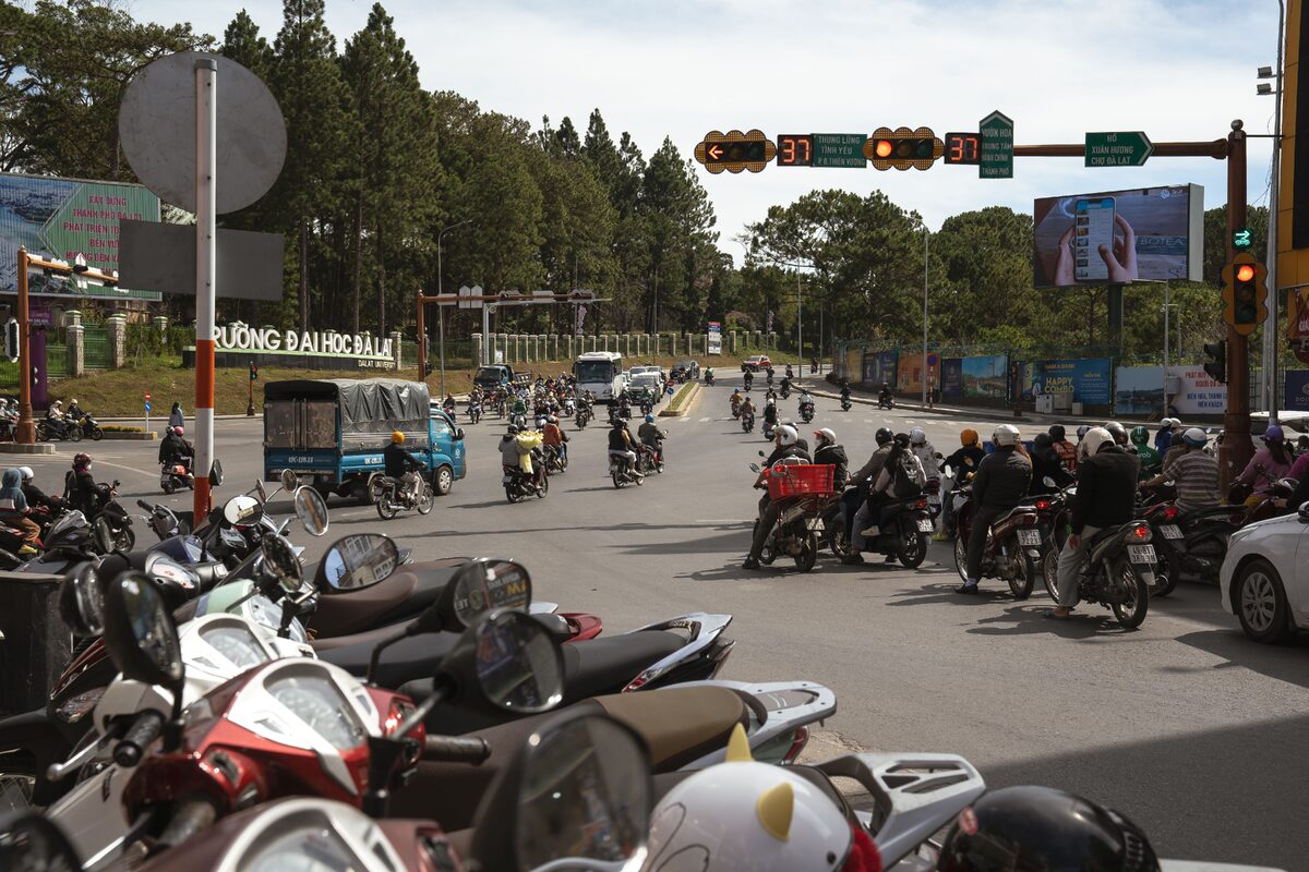 Motorbikes and vehicles navigate a busy intersection in Dalat, Vietnam, showcasing urban life and traffic.