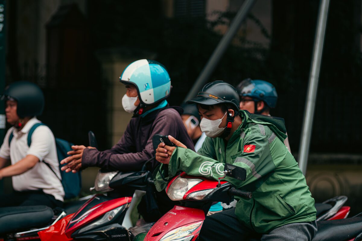 Commuters on motorbikes wearing masks wait in Hanoi, Vietnam traffic, capturing everyday street life.